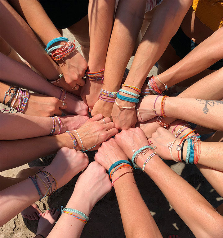 Several hands wearing pura vida bracelets